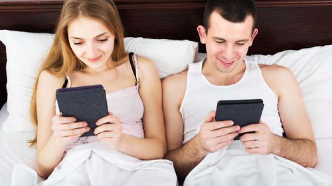 Pasangan asyik ber-gadget di tempat tidur. (Shutterstock)