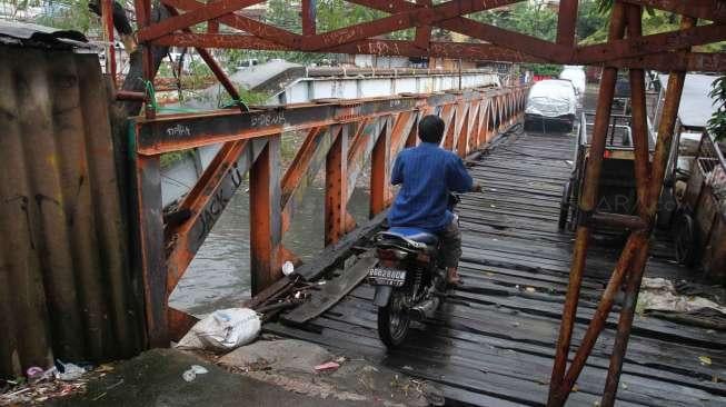 Warga melintasi jembatan yang rusak di Karet, Jakarta, Selasa (18/4).