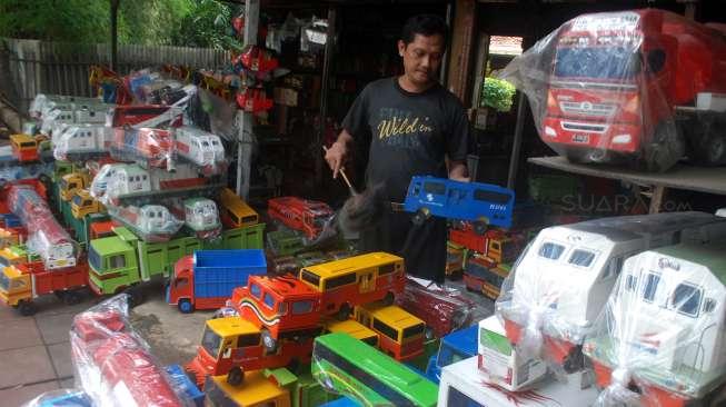 Pelaku Industri Kecil dan Menengah (IKM) menata dagangan berupa replika truk berbahan kayu di Jakarta, Rabu (21/6). [Suara.com/Oke Atmaja]