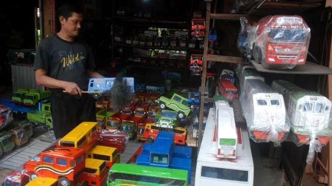 Pelaku Industri Kecil dan Menengah (IKM) menata dagangan berupa replika truk berbahan kayu di Jakarta, Rabu (21/6). [Suara.com/Oke Atmaja]