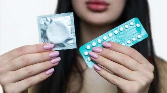 Perempuan memegang alat kontrasepsi kondom dan pil untuk mengendalikan kelahiran. [shutterstock]