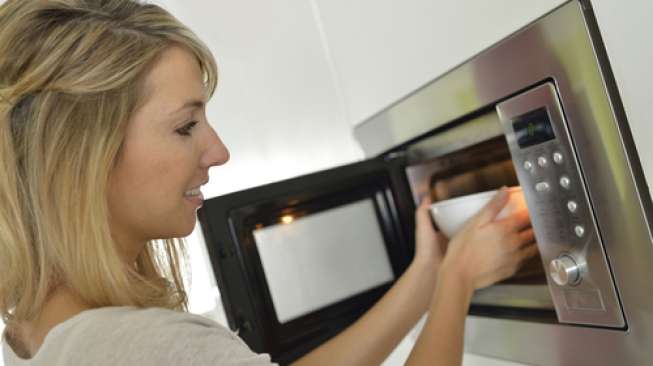 Ilustrasi perempuan sedang memanaskan makanan di microwave (Shutterstock)