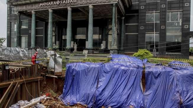 Pekerja LRT memasang terpal plastik untuk menutup area bekas amblas di depan gedung Menara Saidah, Jalan MT. Haryono, Jakarta, Jumat (13/10).