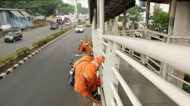 Petugas Penanganan Prasarana dan Sarana Umum (PPSU) terlihat membersihkan salah satu jembatan penyeberangan orang (JPO) sebelum dicat, di Jalan Rasuna Said, Jakarta, Minggu (15/10/2017). [Suara.com/Oke Atmaja]