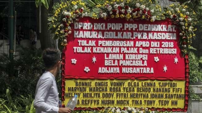 Sebuah karangan bunga bertulisan 'Tolak pemborosan APBD DKI 2018, tolak kenaikan pajak dan retribusi, lawan korupsi, bela Pancasila' terpampang di samping kolam air mancur gedung DPRD DKI Jakarta, Jumat (24/11/2017). [Suara.com/Kurniawan Mas'ud]