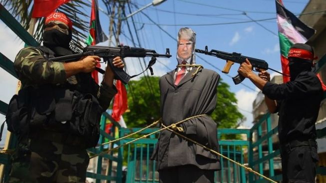 Dua anggota sayap militer Front Rakyat Pembebasan Palestina (FPLP) menodongkan senjata ke boneka Presiden AS Donald Trump dalam aksi protes, 23 Mei 2017. [Mohammed Abed/AFP]