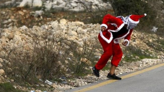 Warga Kristen Palestina memakai pakaian Sinterklas ikut aksi protes dan melempari militer Israel memakai batu, 19 Desember 2017. [AFP]