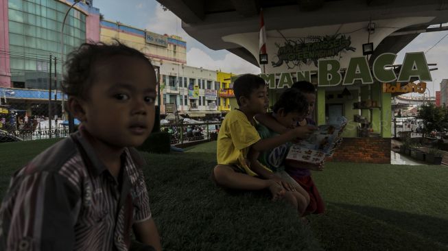 Anak-anak tampak asyik membaca buku di lokasi Taman Baca Kolong Flyover Ciputat, Tangerang Selatan, Provinsi Banten, Kamis (4/1/2018). [Suara.com/Kurniawan Mas'ud]