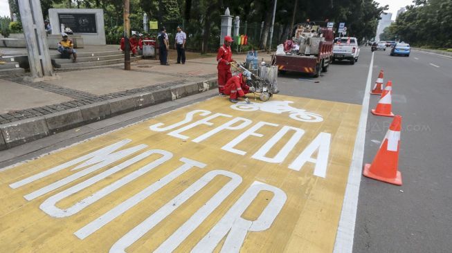 Pekerja mengecat rambu jalur kuning khusus sepeda motor di Jalan Medan Merdeka, Jakarta, Selasa (16/1). 