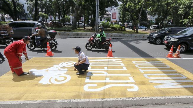 Pekerja mengecat rambu jalur kuning khusus sepeda motor di Jalan Medan Merdeka, Jakarta, Selasa (16/1). 