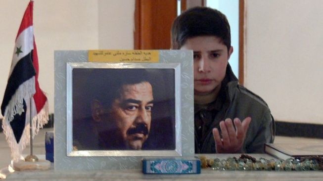 Seorang anak berdoa untuk mendiang Saddam Hussein. [AFP]