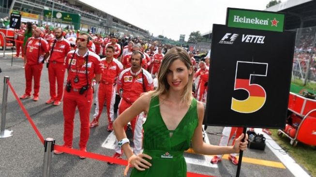 Grid girl tengah berpose di depan pebalap Ferrari, Sebastian Vettel. [AFP/Andrej Isakovic]