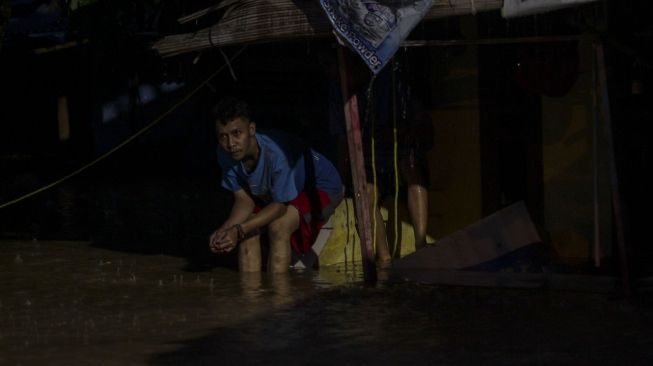 Seorang warga termenung meratapi kediamannya yang dilanda banjir. [suara.com/  Kurniawan Mas'ud]