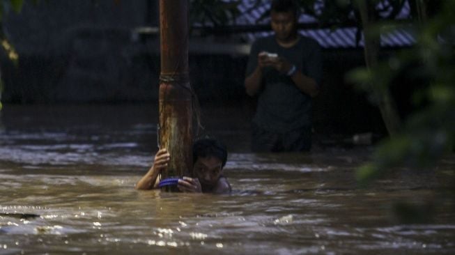 Seorang warga bertahan di tiang listrik saat banjir menerjang Pejaten. [suara.com/ Kurniawan Mas'ud]