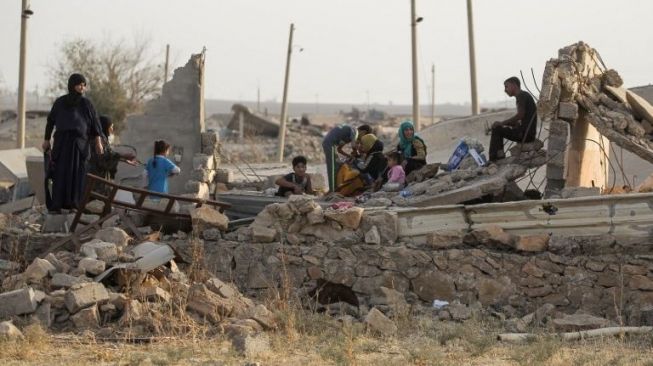 Satu keluarga asal Irak tampak tengah duduk di reruntuhan rumah mereka di desa Barzan, Zummar, Provinsi Nineveh, barat laut Mosul, (27/10/2017). [AFP/Ahmed Al-Rubaye]