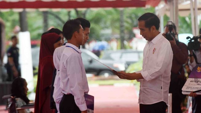 Presiden Joko Widodo (kanan) menyerahkan secara simbolik Kartu Program Keluarga Harapan (PKH) dan Kartu Indonesia Pintar (KIP) di Lapangan Syech Yusuf, Kabupaten Gowa, Sulawesi Selatan, Kamis (15/2). 