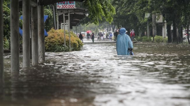 Warga terlihat melintasi genangan air banjir di Cempaka Putih, Jakarta, Kamis (15/2/2018). [Suara.com/Kurniawan Mas'ud]