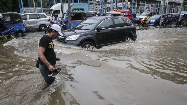 Sejumlah kendaraan dan warga tampak melintasi genangan air banjir di Cempaka Putih, Jakarta, Kamis (15/2/2018). [Suara.com/Kurniawan Mas'ud]