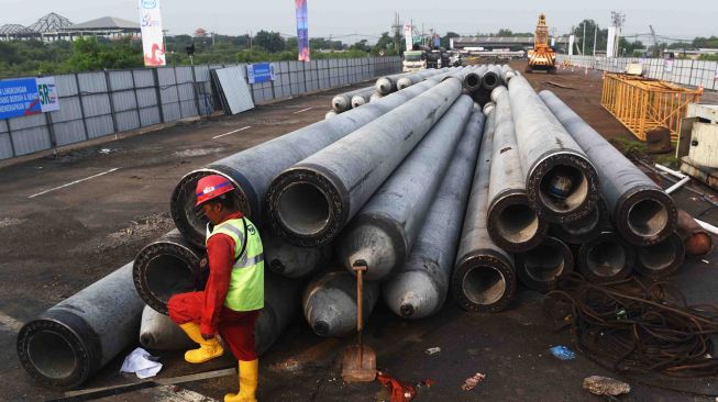 Pekerja melintas di samping tiang pancang saat proses pemancangan pertama pembangunan jalan layang menuju Terminal Teluk Lamong di Surabaya, Jawa Timur, Rabu (7/3).