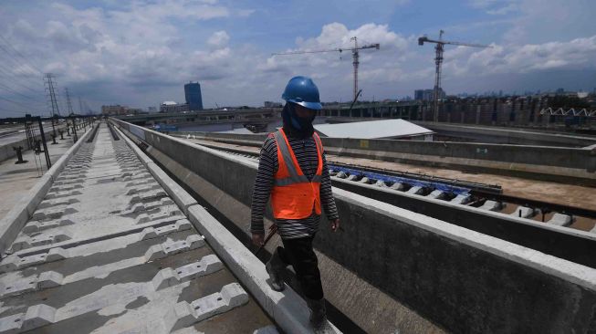 Pekerja melintas di dekat bantalan rel proyek pembangunan infrastruktur depo Light Rail Transit (LRT) di Kelapa Gading, Jakarta, Sabtu (10/3).