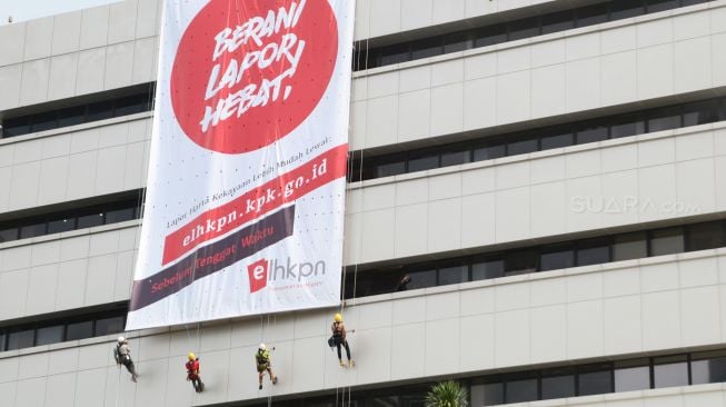 Empat pemanjat profesional membentangkan spanduk yang bertuliskan "Berani Lapor Hebat" di gedung KPK C1 Jalan HR Rasuna Said, Jakarta (26/3).