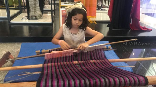 Nantinka Sihombing, putri dari desainer Merdi Sihombing, tampak piawai dalam menenun ulos di area Indonesia Fashion Week (IFW) 2018 di JCC, Rabu (28/3/2018). (Suara.com/Risna Halidi)