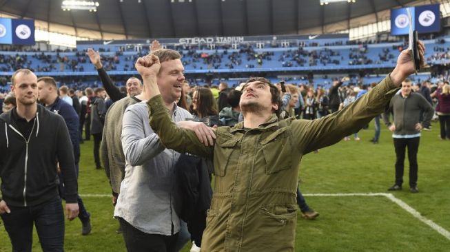 Fans Manchester City menyerbu lapangan Etihad Stadium usai tim kesayangan mereka berpesta gol ke gawang Swansea City, 5-0, Minggu (22/4/2018). [AFP/Oli Scarff]