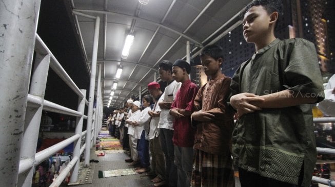 Warga melaksanakan salat Tarawih pertama Ramadan 1439 H di sisi jalan dan jembatan penyeberangan di kawasan Pasar Gembrong, Jatinegara, Jakarta Timur, Rabu (16/5/2018) malam. [Suara.com/Oke Atmaja]