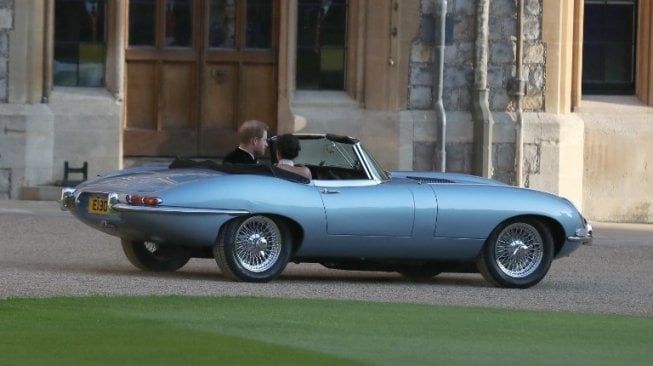 Pangeran Harry dan istrinya Meghan Markle mengendarai mobil Jaguar E-Type bermesin listrik usai menjalani upacara pernikahan di Inggris, Sabtu (19/5). [AFP/Steve Parsons]