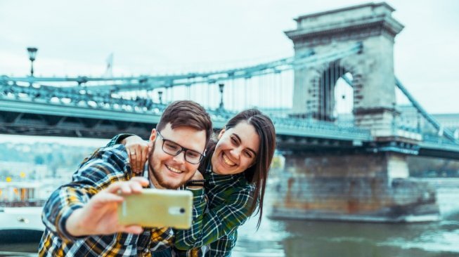 Pasangan traveller tengah wefie berlatarbelakang jembatan klasik [Shutterstock]