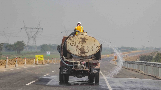 Petugas menyiram jalan yang akan digunakan untuk jalur tol fungsional di kawasan Pemalang-Batang, Jawa Tengah, Kamis (7/6). 