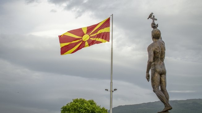 Bendera Makedonia dengan Monument Epiphany di Ohrid, Makedonia [Shutterstock].