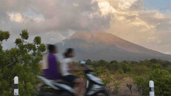 Warga mengendarai sepeda motor dengan latar belakang erupsi Gunung Agung di Desa Datah, Karangasem, Bali, Jumat (29/6). 