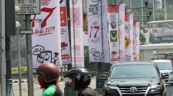 Sejumlah pengendara terlihat melintas di samping spanduk sosialisasi Pemilu Serentak 2019 KPU di kawasan Jalan Imam Bonjol, Jakarta, Selasa (10/7/2018). [Suara.com/Oke Atmaja]