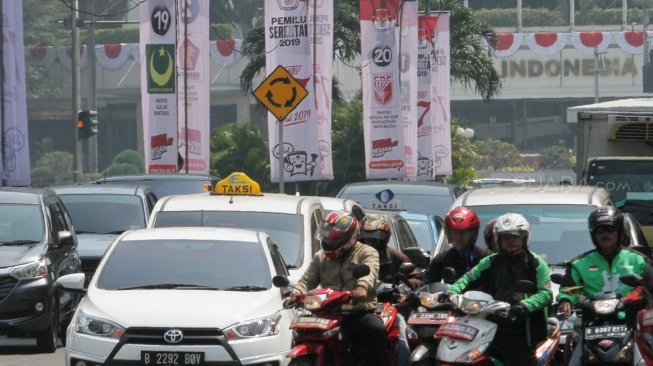 Sejumlah pengendara terlihat melintas di samping spanduk sosialisasi Pemilu Serentak 2019 KPU di kawasan Jalan Imam Bonjol, Jakarta, Selasa (10/7/2018). [Suara.com/Oke Atmaja]