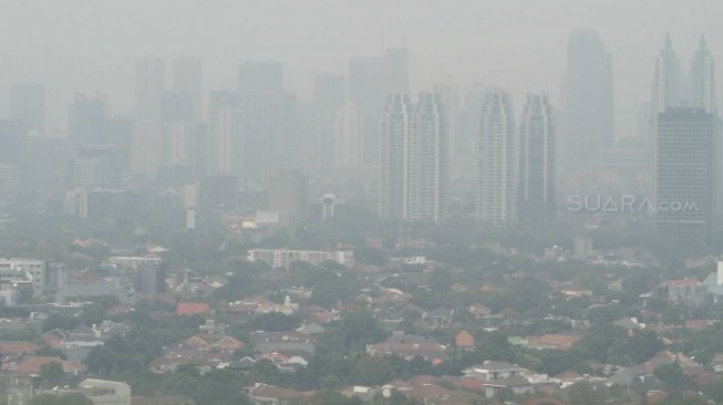 Pemandangan gedung-gedung bertingkat dan kawasan permukiman yang terhalang polusi udara di Jakarta, Jumat (13/7/2018). [Suara.com/Muhaimin A Untung]