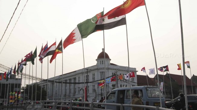 Warga melintas dan beraktivitas di samping deretan bendera negara peserta Asian Games 2018 yang dipasang di kawasan Kali Besar, Kota Tua, Jakarta, Jumat (20/7/2018). [Suara.com/Muhaimin A Untung]