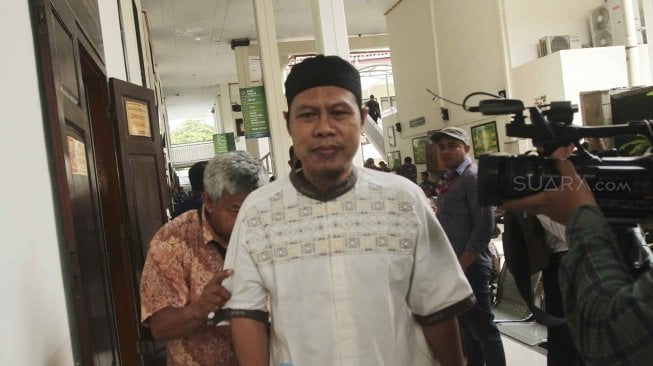 Pimpinan JAD Zainal Anshori alias Abu Fahry alias Qomaruddin bin M Ali dengan pengawalan petugas kepolisian bersiap mengikuti sidang perdana pembubaran Jamaah Ansharut Daulah (JAD) di Pengadilan Negeri Jakarta Selatan, Jakarta, Selasa (24/7). Dalam sidang tersebut, JAD didakwa sebagai kelompok yang menggerakan teror di Indonesia dan telah menyebabkan jatuhnya korban jiwa dan kerusakan objek vital. (Suara.com/ Muhaimin A Untung). 