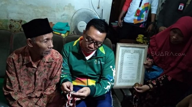 Menpora Imam Nahrawi (tengah) tengah melihat medali yang pernah diraih mantan atlet berprestasi paralimpian Indonesia, Soeharto (kiri), dalam kunjungan ke rumah sang atlet di Surabaya, Jawa Timur, Selasa (24/7/2018). [Suara.com/Dimas Angga P]