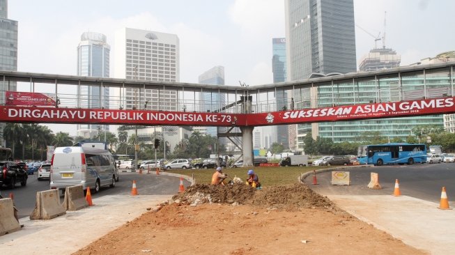 Sejumlah kendaraan melintasi Jembatan Penyebrangan Orang (JPO) di Bundaran HI, Jakarta, Rabu (25/7). Gubernur DKI Jakarta Anies Baswedan berencana akan melakukan pembongkaran JPO Bundaran HI agar tidak menganggu patung selamat datang yang dibangun untuk menyambut peserta Asian Games. Nantinya usai dirobohkan, dilokasi tersebut akan dibangun 'Pelican Crossing' untuk memudahkan pejalan kaki menyeberang jalan. [suara.com/Oke Dwi Atmaja]