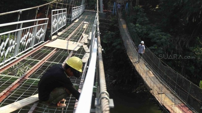 Sejumlah pekerja menyelesaikan pembuatan jembatan gantung di RW 002 Kelurahan Srengseng Sawah, Jagakarsa, Jakarta Selatan, Sabtu (28/7). Pemrov DKI Jakarta bekerjasama dengan PT Wiratman dengan menggunakan dana CSR membangun jembatan permanen untuk mengganti jembatan gantung "indiana jones" yang tidak layak untuk digunakan warga. [suara.com/Muhaimin A Untung]
