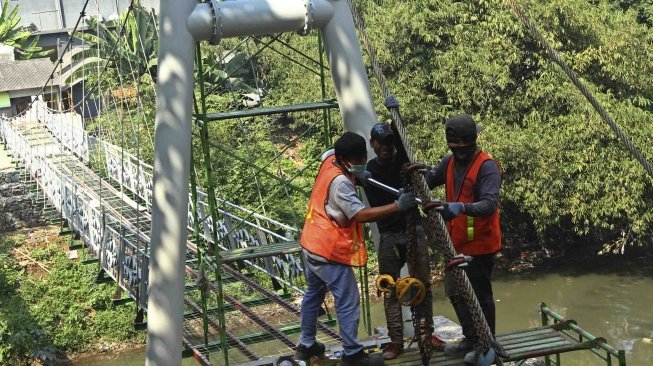 Sejumlah pekerja menyelesaikan pembuatan jembatan gantung di RW 002 Kelurahan Srengseng Sawah, Jagakarsa, Jakarta Selatan, Sabtu (28/7). Pemrov DKI Jakarta bekerjasama dengan PT Wiratman dengan menggunakan dana CSR membangun jembatan permanen untuk mengganti jembatan gantung "indiana jones" yang tidak layak untuk digunakan warga. [suara.com/Muhaimin A Untung]
