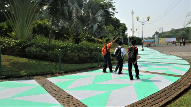 Warga melintas di Trotoar kawasan Monumen Nasional yang sudah di cat, Jakarta, Selasa (31/7). Pengecatan trotoar atau fasilitas pejalan kaki ini untuk mempercantik kawasan silang Monas dalam menyambut pagelaran Asian Games 2018 yang akan berlangsung Agustus hingga September 2018 mendatang.[suara.com/Muhaimin A Untung]