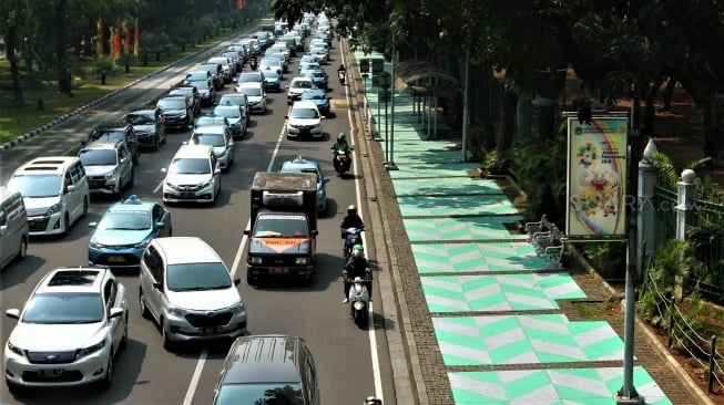 Warga melintas di Trotoar kawasan Monumen Nasional yang sudah di cat, Jakarta, Selasa (31/7). Pengecatan trotoar atau fasilitas pejalan kaki ini untuk mempercantik kawasan silang Monas dalam menyambut pagelaran Asian Games 2018 yang akan berlangsung Agustus hingga September 2018 mendatang.[suara.com/Muhaimin A Untung]