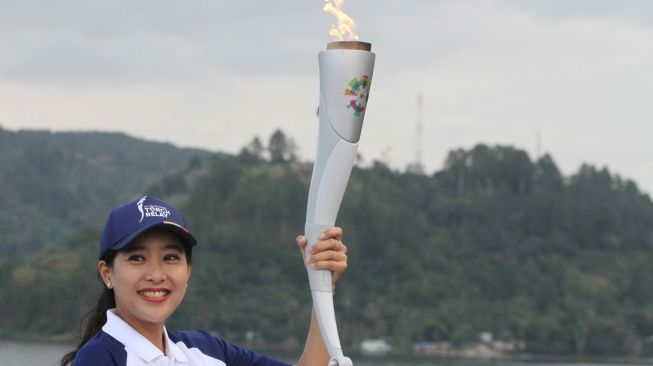 Artis Olivia Zalianty memegang obor Asian Games 2018 dengan latar belakang Danau Toba, Simalungun, Sumatera Utara, Rabu (1/8). [Antara/Lazuardy Fahmi]