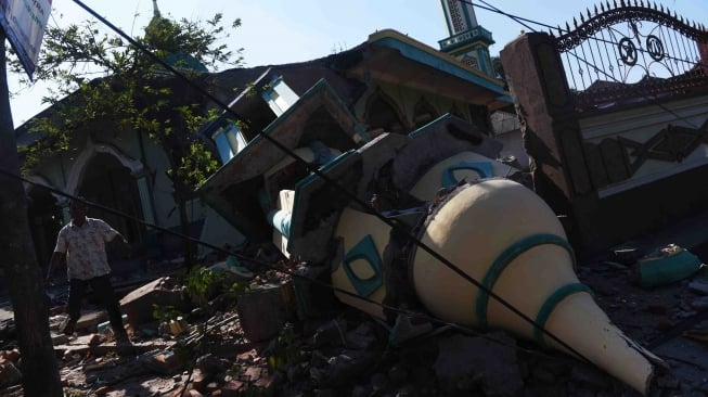 Warga melintas di samping masjid yang rusak akibat gempa bumi, Pemenang, Lombok Utara, NTB, Senin (6/8). BNPB mencatat sedikitnya 91 orang korban meninggal dunia akibat bencana gempa bumi yang terjadi Minggu (5/8) dan terdapat kemungkinan akan bertambah. ANTARA FOTO/Zabur Karuru