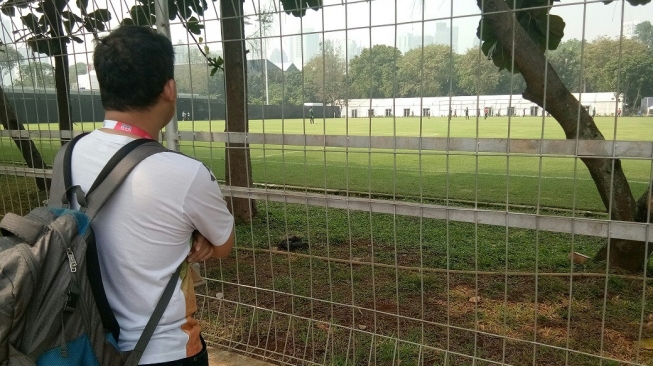 Seorang jurnalis melihat dari luar latihan Timnas Indonesia U-23 jelang melawan Taiwan di lapangan A Senayan, Jakarta, Sabtu (11/8/2018) [Suara.com/Adie Prasetyo]