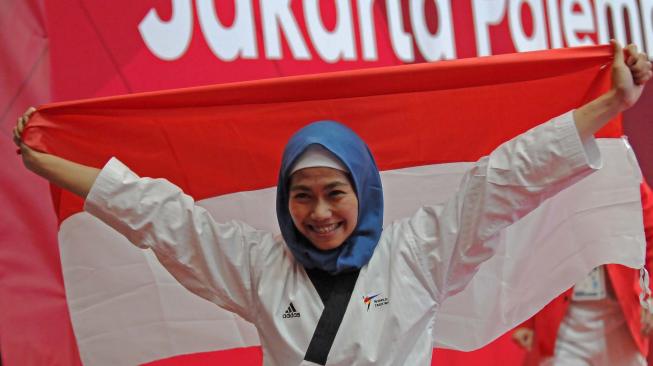 Defia Rosmaniar melakukan selebrasi dengan membawa bendera merah putih atas kemenangannya dalam pertandingan taekwondo nomor poomsea tunggal putri pada Asian Games 2018 di Jakarta Convention Center (JCC), Minggu (19/8). ANTARA FOTO/INASGOC/Sunyoto