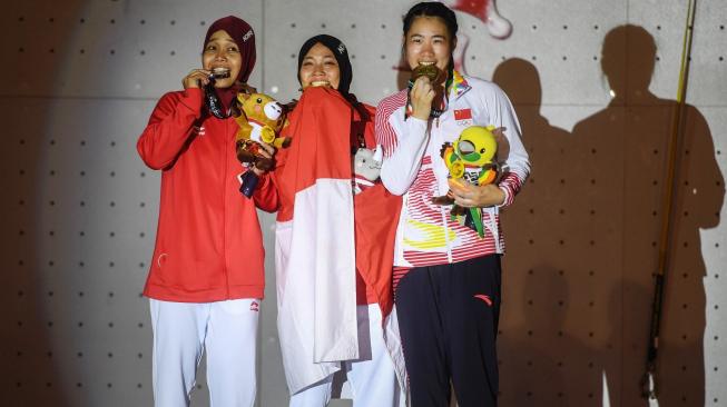 Atlet panjat tebing Indonesia peraih medali emas, Aries Susanti Rahayu (tengah), bersama Puji Lestari (kiri) dan atlet Cina, He Cuilian, usai penganugerahan medali kategori speed putri Asian Games 2018 di Arena Panjat Tebing Jakabaring Sport City (JSC), Palembang, Kamis (23/8/2018). [Antara/INASGOC/Hendra Nurdiyansyah]