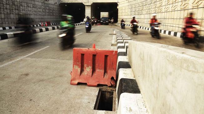 Kendaraan melintas di samping penutup saluran air atau "steel grating" yang hilang di jalur Lintas Bawah Mampang-Kuningan, Jakarta, Sabtu (25/8). [Suara.com/Muhaimin A Untung]